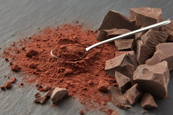 在干可可粉堆和灰色表面的有机巧克力堆上排列光亮茶匙 — 图库照片