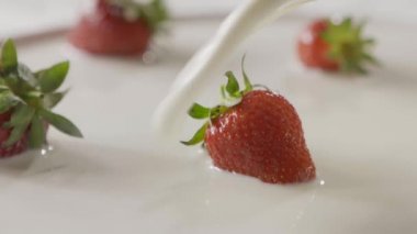 Slow motion of a falling splash of milk to the ripe red strawberries on plate. On a white plate is few berries in the milk. Close-up background, soft focus. Full HD video 
