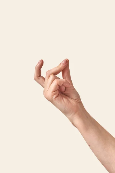 Female hand making finger snap gesture or holding invisible tiny object looking up isolated on cream or beige background. Soft grab action woman hand.