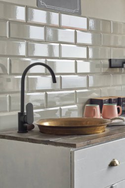 Eski bakır lavabo, gri fayanslı duvarlı, dolaplı, ahşap tezgahta pembe bardaklı küçük mutfaklı bir ev. Kır evi mutfak konsepti.