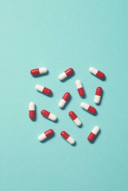 Turkuaz zemin üzerine serpiştirilmiş kırmızı ve beyaz ilaç hapları. Kopyalama alanı olan düz.