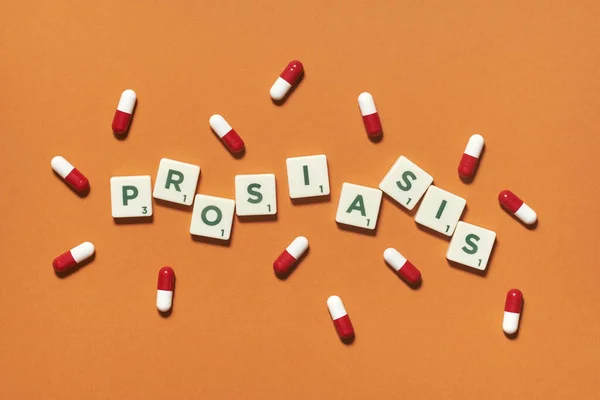 Psoriasis word formed of scrabble blocks and pharmaceutical pills strewn over orange backdrop. Skin disease and medical treatment concept.