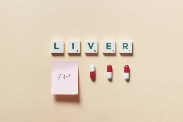 薬の丸薬とベージュの背景に朝の薬の時間と付箋でスクラブルブロックで形成された肝臓の単語 肝臓の状態と身体の健康意識 — ストック写真