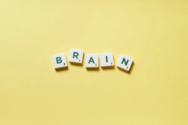 Brain word formed of scrabble tiles on yellow background.
