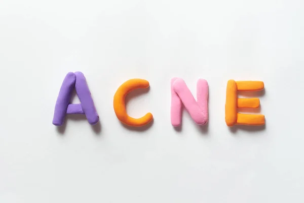 Acne word formed of vivid plasticine on white background. Skin disease and medical treatment concept.