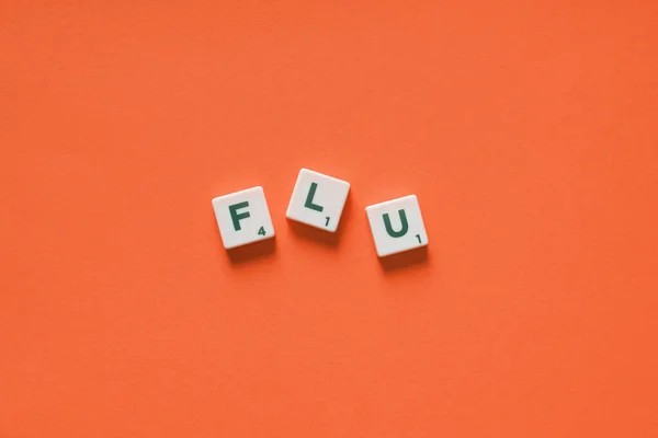 Flu word formed of messy scrabble tiles on orange backdrop. Virus infection and medical treatment concept.