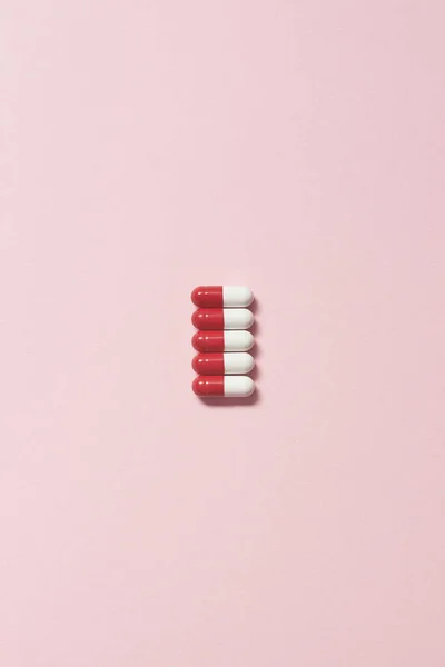 红色和白色的药物胶囊整齐地铺在粉红色的背景上 保健和药物辅助治疗 — 图库照片