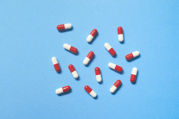 红色和白色的药物胶囊散布在蓝色背景 复制空间 保健和药物辅助治疗 — 图库照片