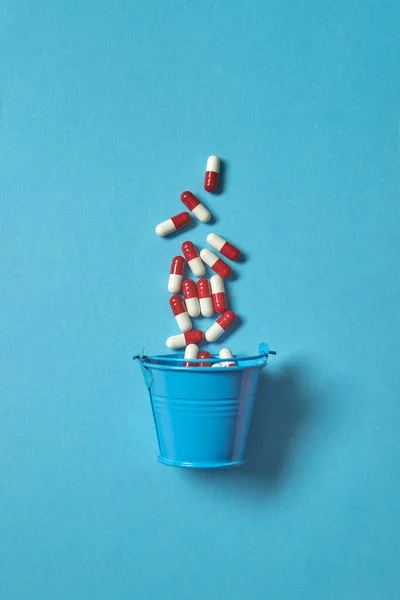 薬の丸薬が青い背景でバケツから落ちる コピースペース付きのトップビュー — ストック写真