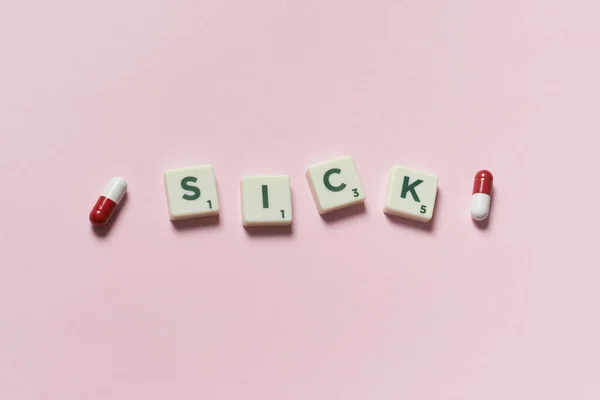 Ziek Woord Gevormd Door Scrabble Blokken Farmaceutische Pillen Roze Achtergrond — Stockfoto