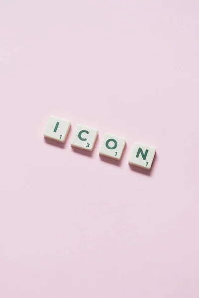 Icon word formed of scrabble tiles on pink background. Creative template with copy space.