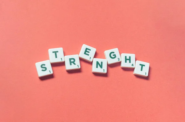 Strength word formed of scrabble blocks on red background. Creative template with copy space.