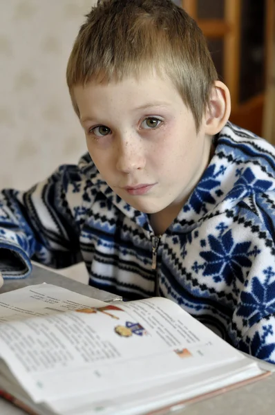 The 10-year-old boy with tears in the eyes sits before the textb — Stock Photo, Image