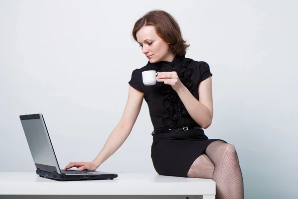 Zittend op de tafel een meisje met een laptop en een kopje koffie — Stock Fotó