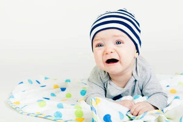 Χαριτωμένο μωρό με ριγέ καπέλο ξαπλωμένοs κάτω επάνω σε μια κουβέρτα — Φωτογραφία Αρχείου