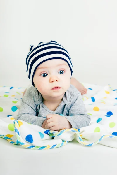 Niedliches Baby mit gestreiftem Hut auf einer Decke liegend — Stockfoto