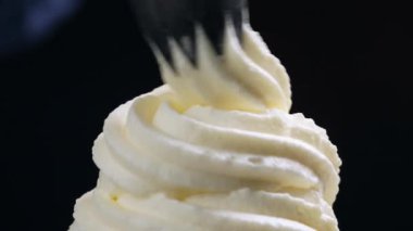 Krem şantiyi siyah arka planda döndürmek için aşçı kremayı dekorasyon çantasından sıkar. 