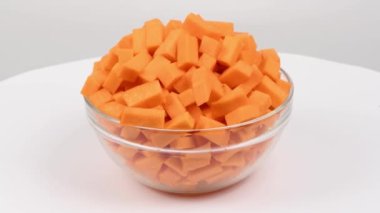 Bir cam kasede dilimlenmiş tereyağı ezmesi (Cucurbita moschata, tereyağlı balkabağı veya gitar büyükannesi) beyaza izole edilmiş. Yan görüş. Döngü hareketi. Rotasyon 360. 4K UHD video görüntüsü 3840X2160.