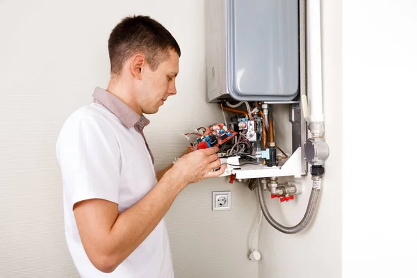 Encanador anexa tentando corrigir o problema com o equipamento de aquecimento residencial. Reparação de uma caldeira a gás — Fotografia de Stock