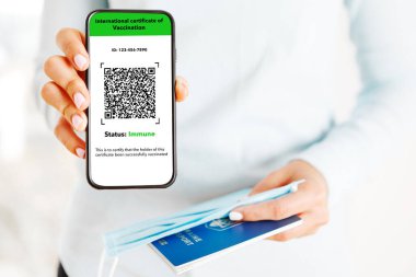Cep telefonunu elinde tutan kadın bir elinde dijital aşı sertifikası, diğer elinde pasaport, maske ve bilet vardı.