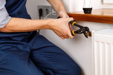 Isıtma radyatörünü tamir et. Adam ingiliz anahtarıyla radyatör onarıyor. Radyatörden hava çekiliyor.