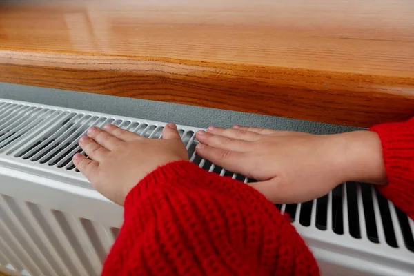 Una niña se calienta las manos y los pies en un radiador — Foto de Stock