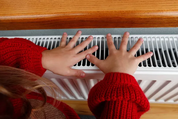 Una niña se calienta las manos y los pies en un radiador — Foto de Stock