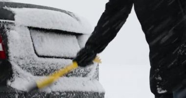 Genç adam kış günü dışarıda arabadan kar temizliyor.