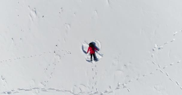 Lycklig kvinna ligger i snön och gör en ängel — Stockvideo