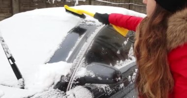 Genç bir kadın kış günü açık havada arabadan kar temizliyor.