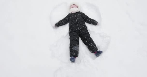 Menina feliz encontra-se na neve e faz um anjo — Vídeo de Stock