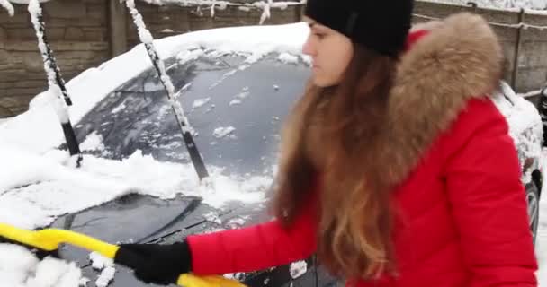 Ung kvinna rengöring snö från bilen utomhus på vinterdagen — Stockvideo