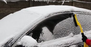 Genç bir kadın kış günü açık havada arabadan kar temizliyor.