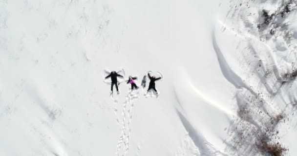 Gelukkig familie vrouw en man ligt in de sneeuw en maakt een engel — Stockvideo