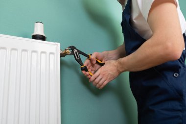 Isıtma radyatörünü tamir et. Adam ingiliz anahtarıyla radyatör onarıyor.. 