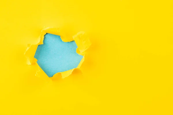 Geel en blauw gat in het papier met gescheurde zijkanten. — Stockfoto