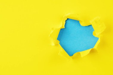 Yırtık kenarlı kağıttaki sarı ve mavi delik.