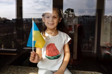 Elinde Ukrayna bayrağı olan kız pencereden dışarı bakıyor.