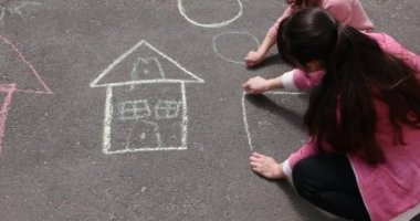 Küçük bir kız kaldırıma tebeşirle bir ev çiziyor..