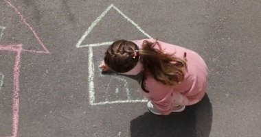 Küçük bir kız kaldırıma tebeşirle bir ev çiziyor..