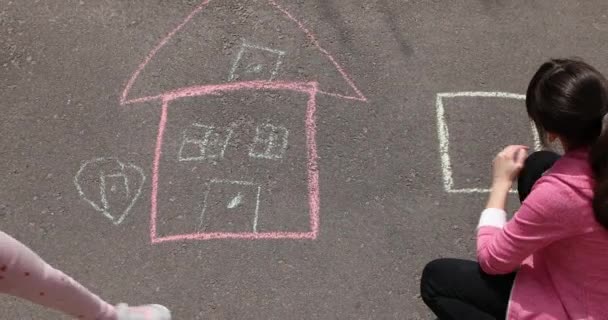 Een klein meisje tekent een huis met krijt op de stoep. — Stockvideo