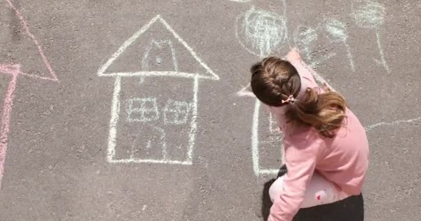Een klein meisje tekent een huis met krijt op de stoep. — Stockvideo