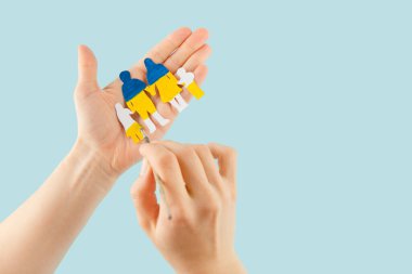 Kadın elleri Ukrayna 'nın ulusal renklerinde boyanmış kağıt kesiği bir aileyi tutuyor..