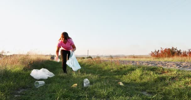 Девушка-волонтёр собирает мусор в мусорном мешке на природе. — стоковое видео