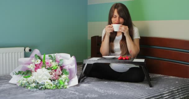 Souriant fille mignonne avec des fleurs dans ses mains en pyjama assis sur le lit — Video