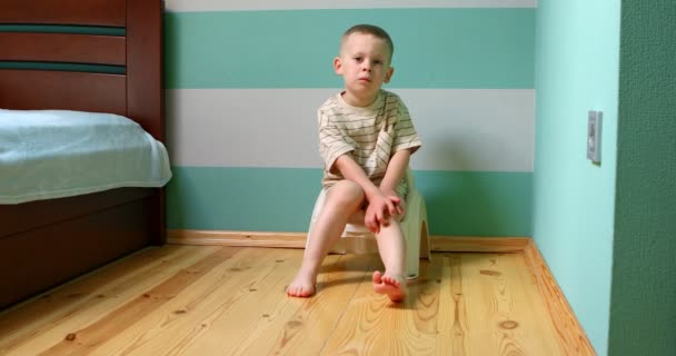 Junge auf Töpfchen an weißer Wand blickt direkt in die Kamera. — Stockvideo