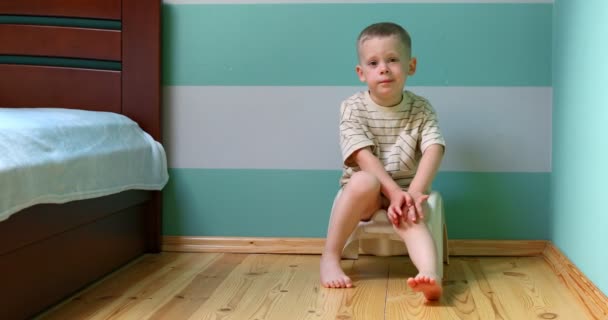 Boy on a potty against white wall looking straight to the camera. — Stock Video