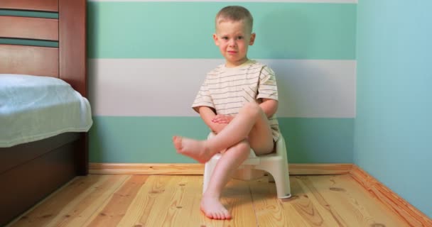 Chlapec na nočník proti bílé zdi dívá přímo do kamery. — Stock video