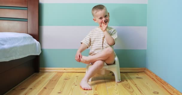 Boy on a potty against white wall looking straight to the camera. — Stock Video