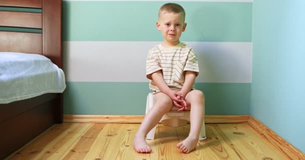 Pojke på en potta mot vit vägg tittar rakt in i kameran. — Stockvideo